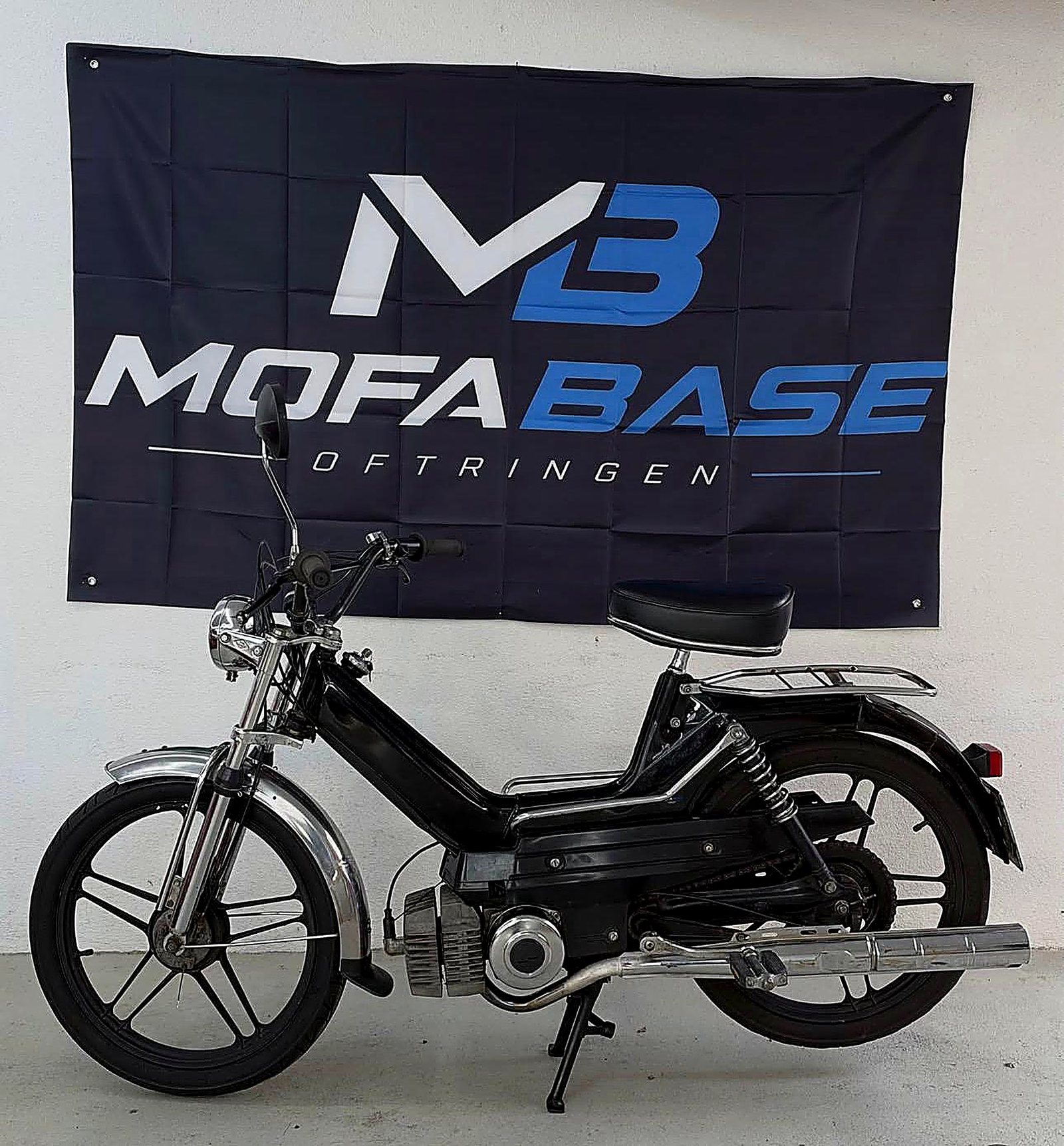Schwarzes Puch Maxi vor dem Mofabase-Banner